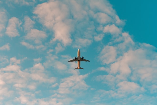 view from below of plane flying in blue sky and clouds